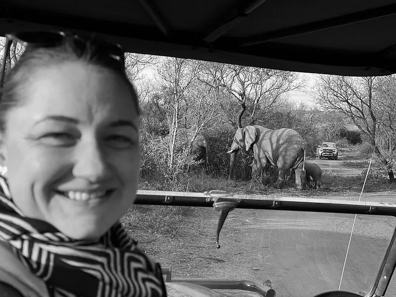 Annelize on safari, with elephants on the road behind her